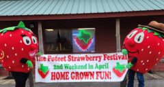 Two lifesize strawberry costumes holding a sign that says "The Poteet Strawberry Festival. 2nd Weekend in April. Home Grown Fun" standing in front of a building